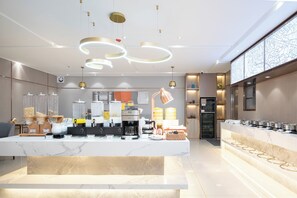 A modern hotel lobby with a marble reception desk, coffee machines, and a large digital map display.