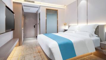 Una habitación de hotel moderna con una cama grande, mesitas de noche, un televisor de pantalla plana y un vestidor.