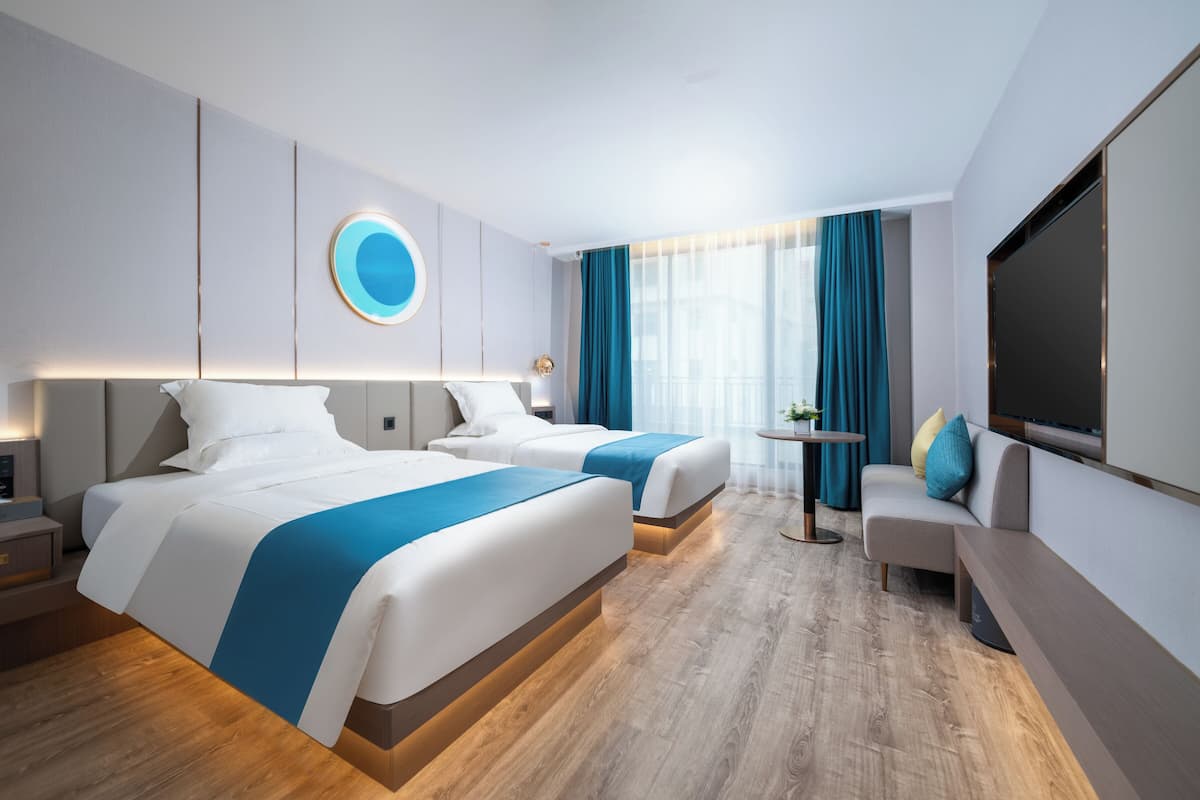 Moderni hotellihuone, jossa on kaksi sänkyä, sohva, televisio ja pieni pöytä.
