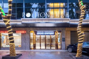 A hotel entrance with a service apartment sign, a glass facade, and a car parked outside.