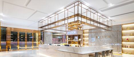 A modern hotel lobby with a central bar area, marble flooring, and a glass partition.