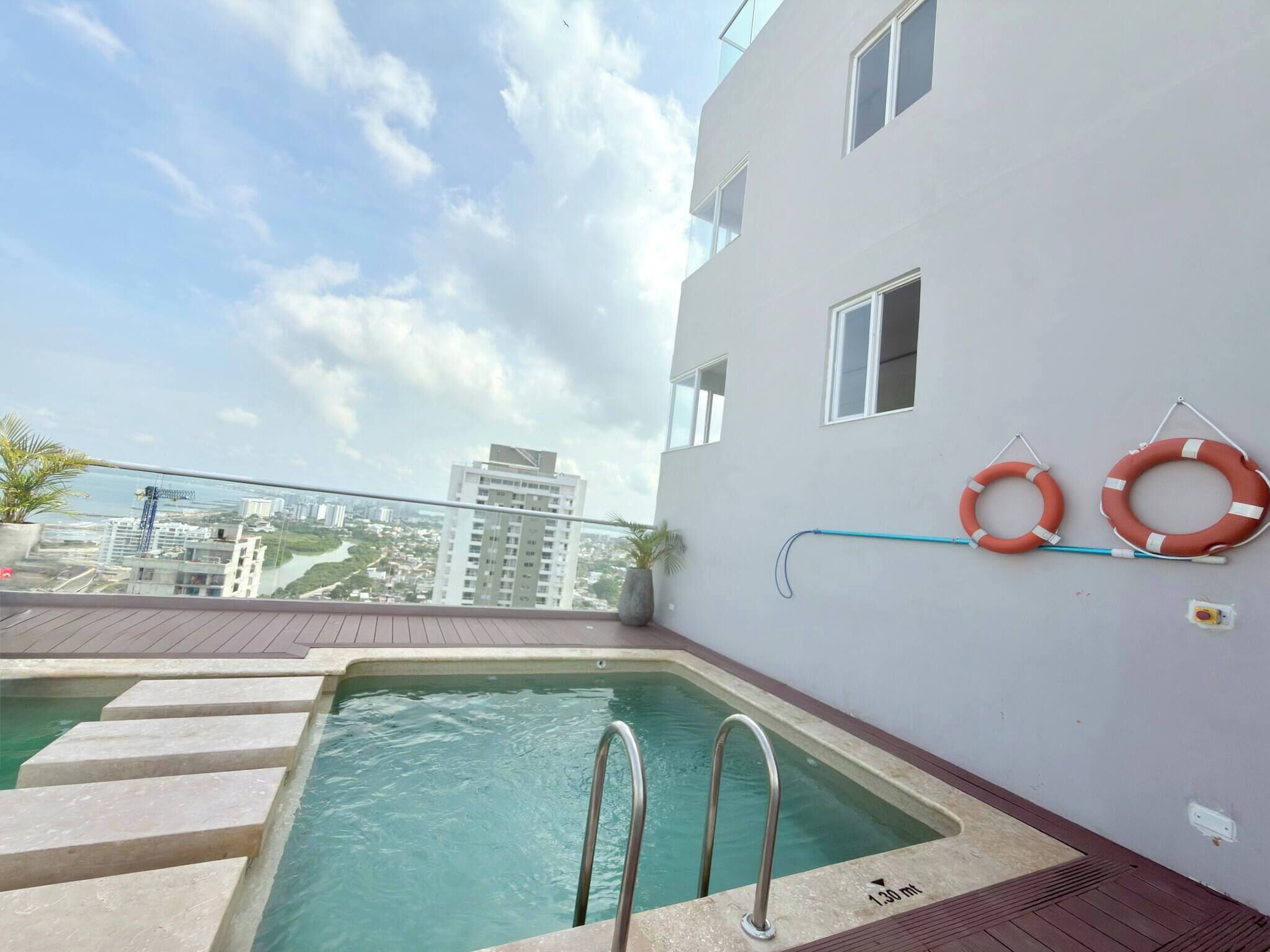 A rooftop pool with a view of the cityscape, a lifebuoy, and a water slide.
