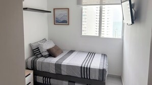 A bedroom with a bed, a ceiling fan, a window with a view of buildings, and a mounted TV. - Exclusive 3 Bedroom Apartment - Sunset 47 (Cartagena)