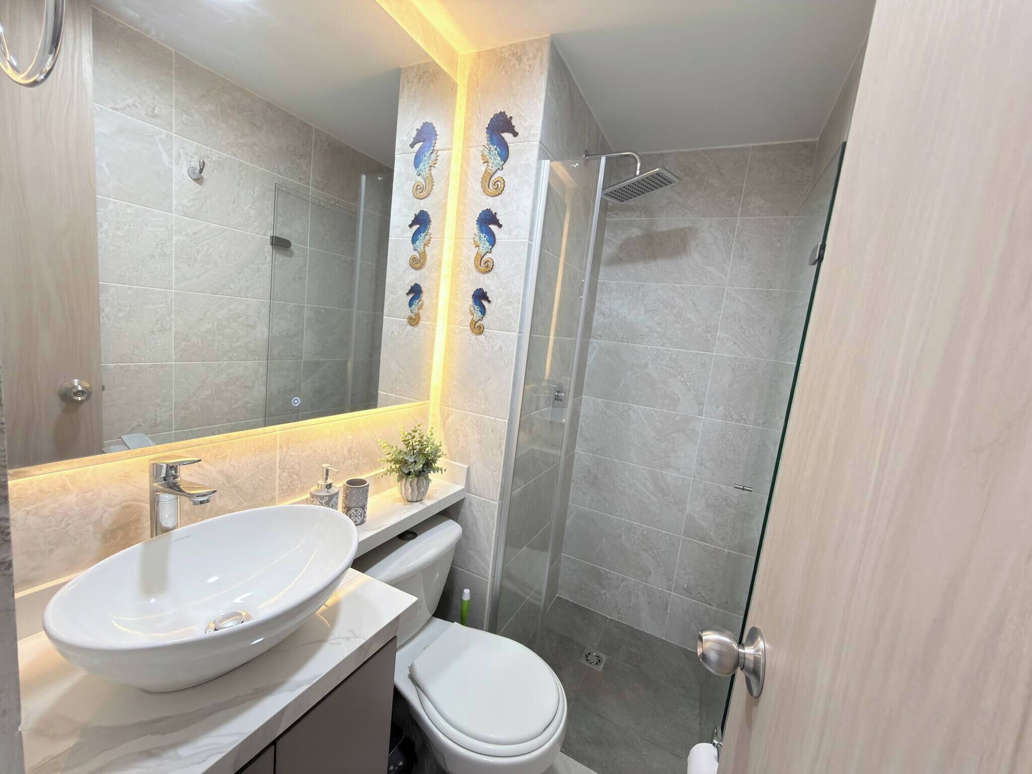 A modern bathroom with a large mirror, a vessel sink, a toilet, and a glass-enclosed shower.