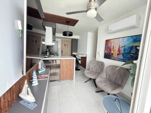 Una cocina moderna con una isla central, un área de comedor con dos sillas, un ventilador de techo y un cuadro en la pared.