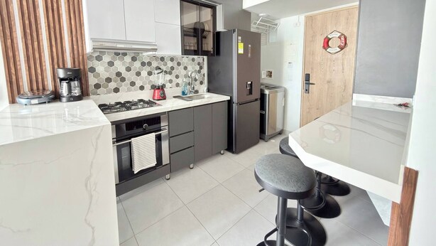 A modern kitchen with a central island, a built-in oven, a refrigerator, and a coffee maker. - Exclusive 3 Bedroom Apartment - Sunset 47 (Cartagena)