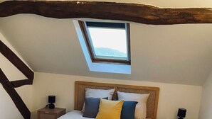 A bedroom with a large bed, wooden headboard, two bedside tables, a skylight, and wooden flooring. - Gîte des Charbonneaux (Avrée)