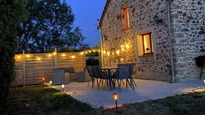 A stone building with a tiled roof, a wooden fence, and outdoor seating. - Gîte des Charbonneaux (Avrée)