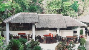 A covered outdoor seating area with tables and chairs, surrounded by lush greenery. - Avana Hills Boracay Prime - Grand (Boracay Island)