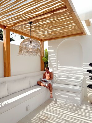 A person sitting on a white sofa under a wooden pergola with a woven light fixture, in a room with white walls and a large window. - Designer 2BR Private Pool Villa Near Nyang Nyang Beach Uluwatu (kuta selatan)
