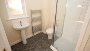 Un baño con lavamanos blanco, inodoro y cabina de ducha con mampara de cristal.