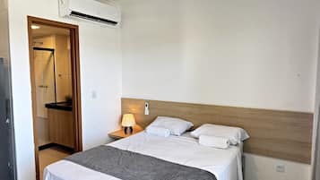 Quarto de hotel com cama, mesa de cabeceira, luminária e ar condicionado.