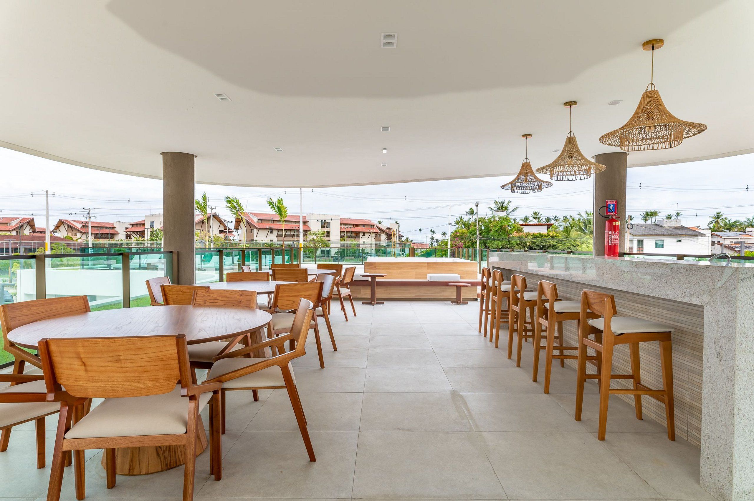 A rooftop bar with wooden tables and chairs, a bar counter, and hanging wicker lamps.