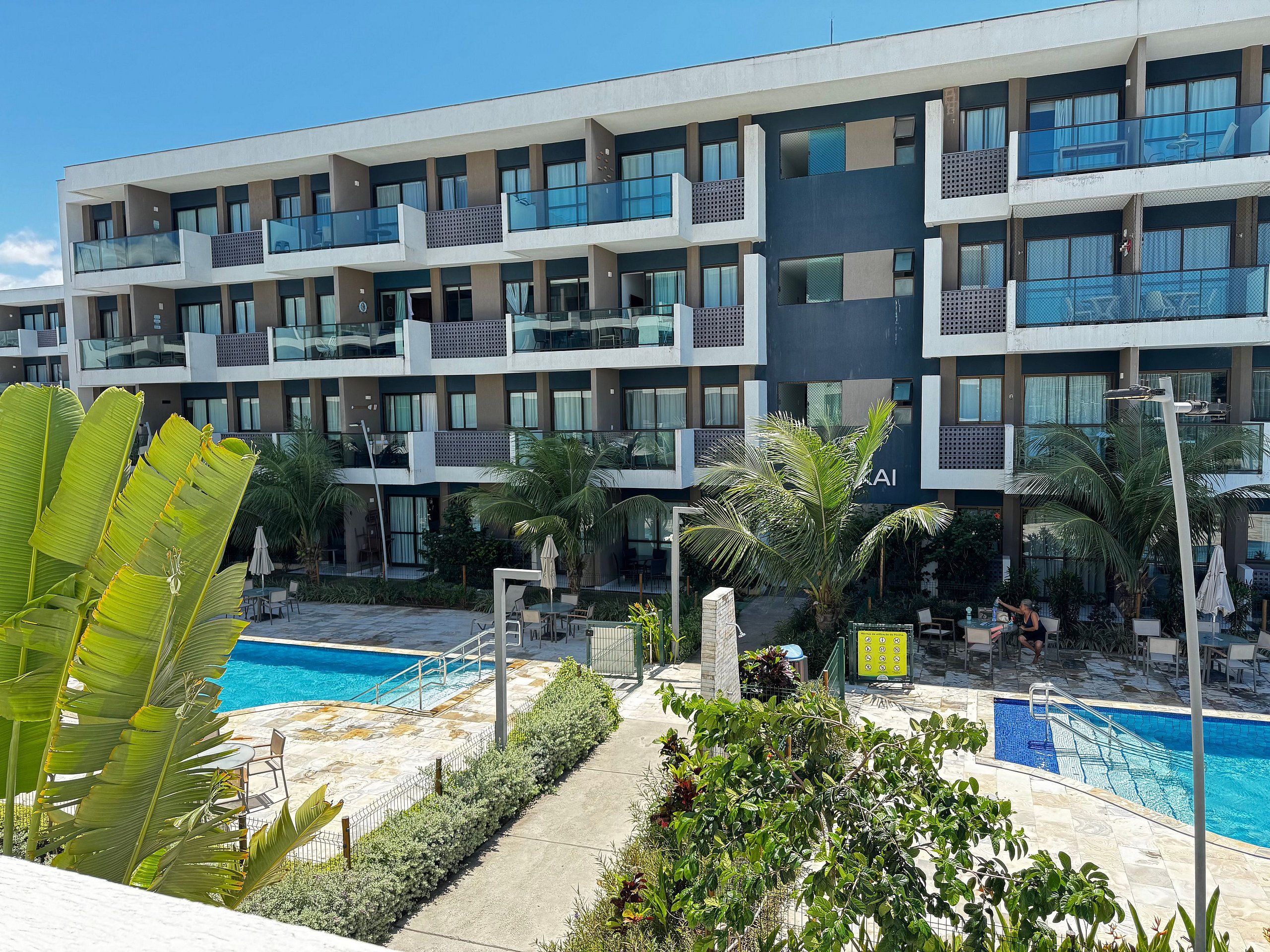 A modern hotel with multiple balconies, a swimming pool, and lush greenery.