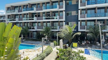 A modern hotel with multiple balconies, a swimming pool, and lush greenery.