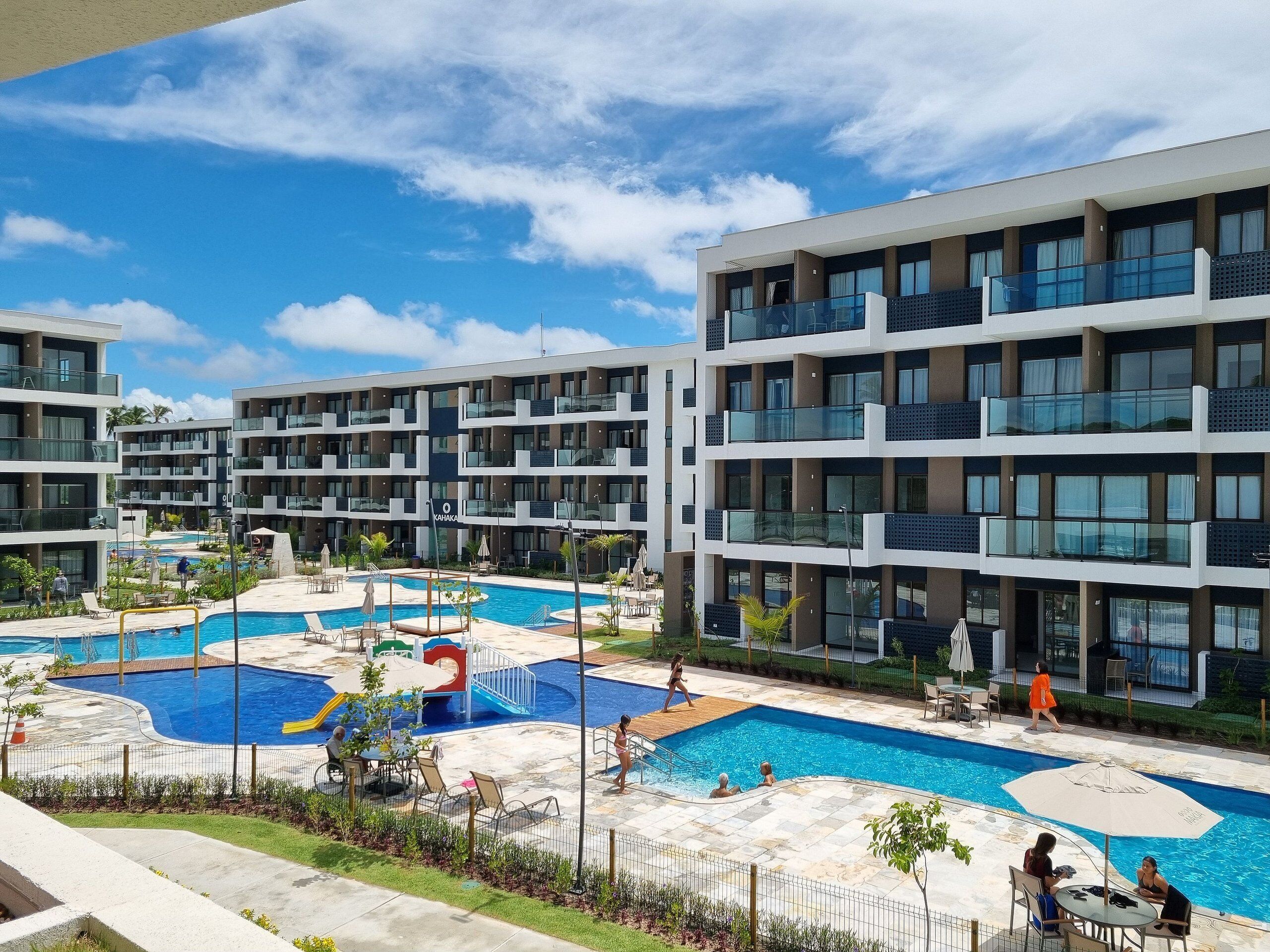 Um hotel moderno com várias varandas, uma piscina central e uma área de piscina ajardinada.