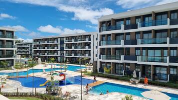 Um hotel moderno com várias varandas, uma piscina central e uma área de piscina ajardinada.