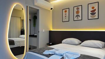 A modern hotel room with a large bed, a bedside table, a mirror, and wall-mounted artwork.