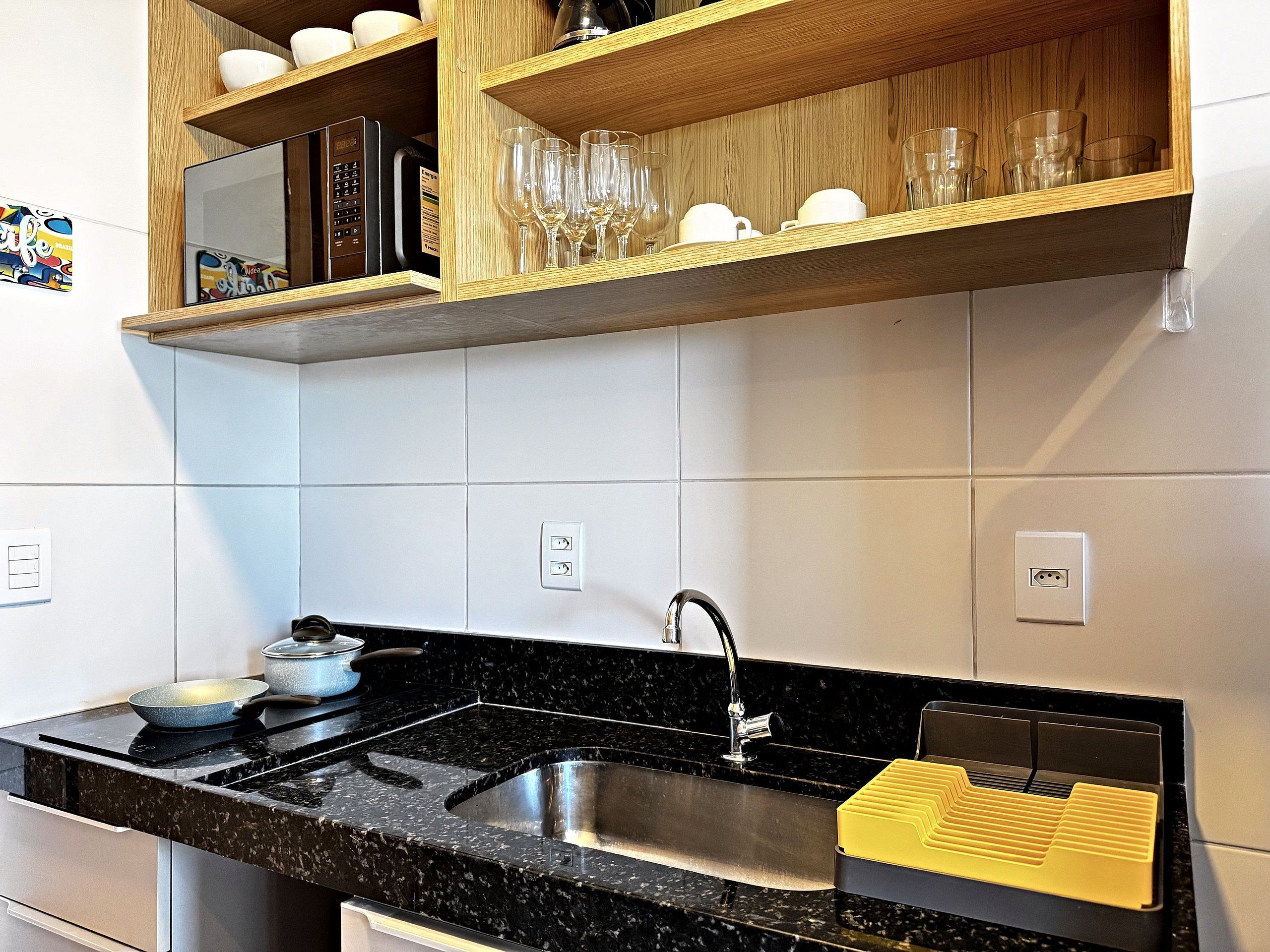A kitchen with a black countertop, stainless steel sink, and wooden shelves above.