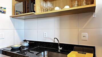 A kitchen with a black countertop, stainless steel sink, and wooden shelves above.