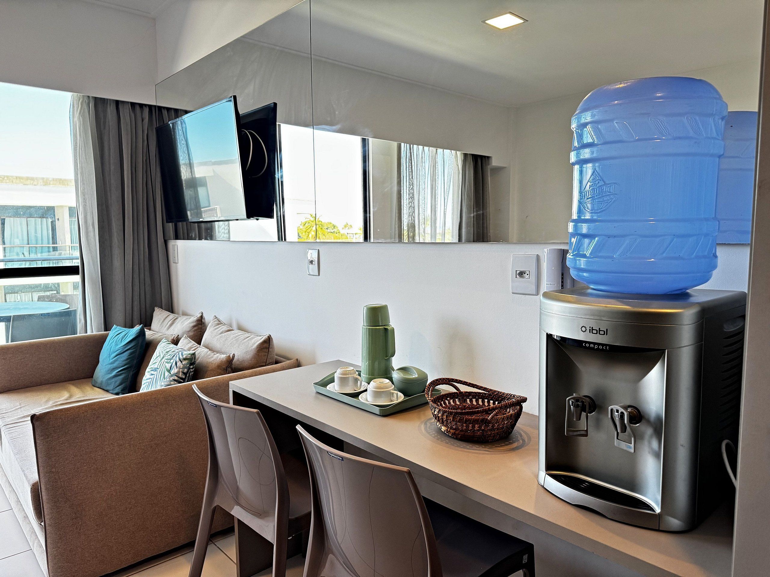 A modern kitchenette with a water dispenser, a coffee maker, and a seating area with a sofa and chairs.
