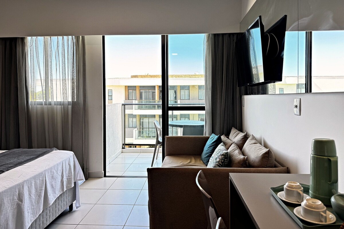 Habitación de hotel con cama, sofá, mesa de comedor y televisor en la pared.