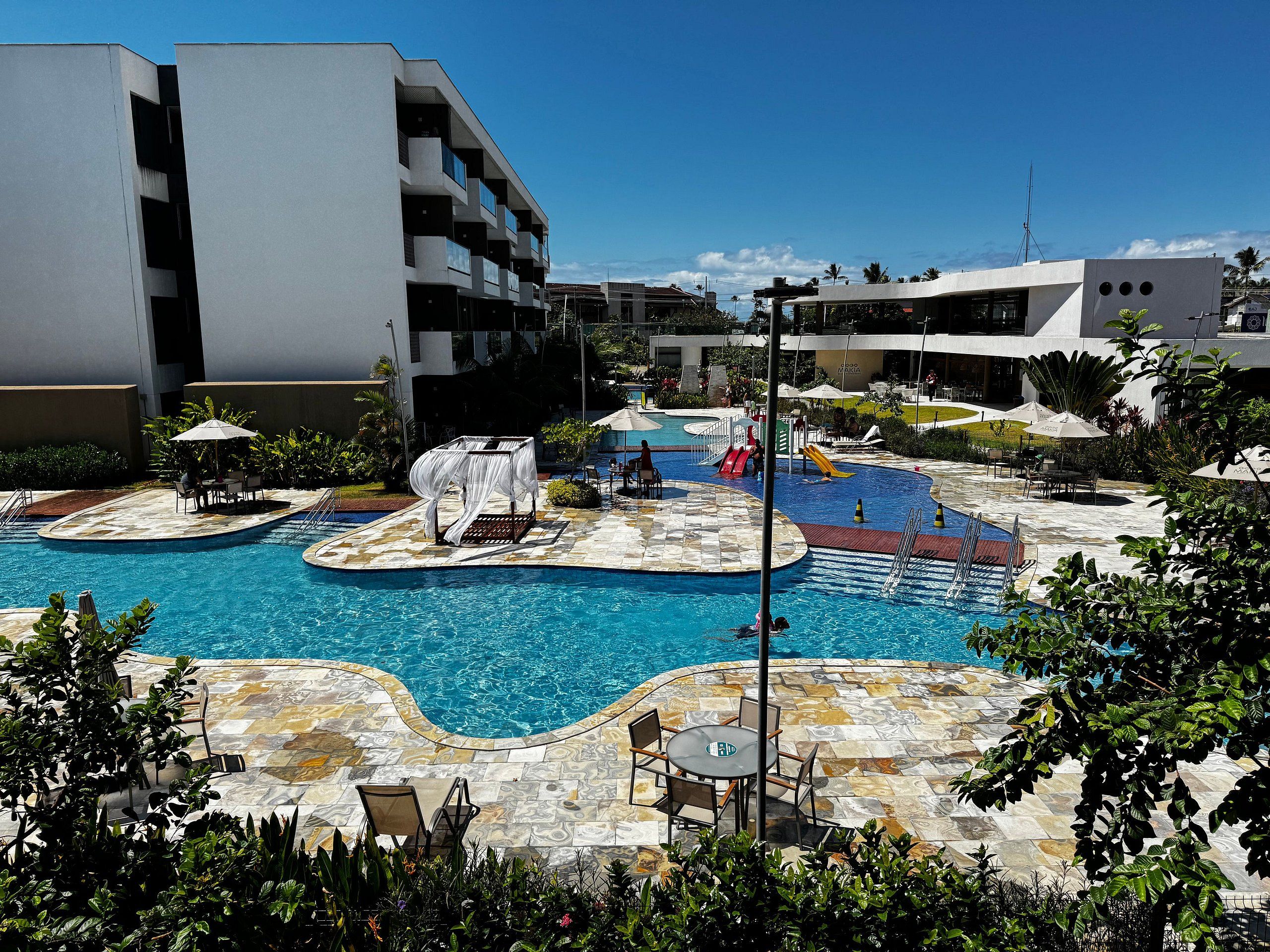 Ein Schwimmbadbereich mit mehreren Pools, Liegestühlen und Sonnenschirmen.