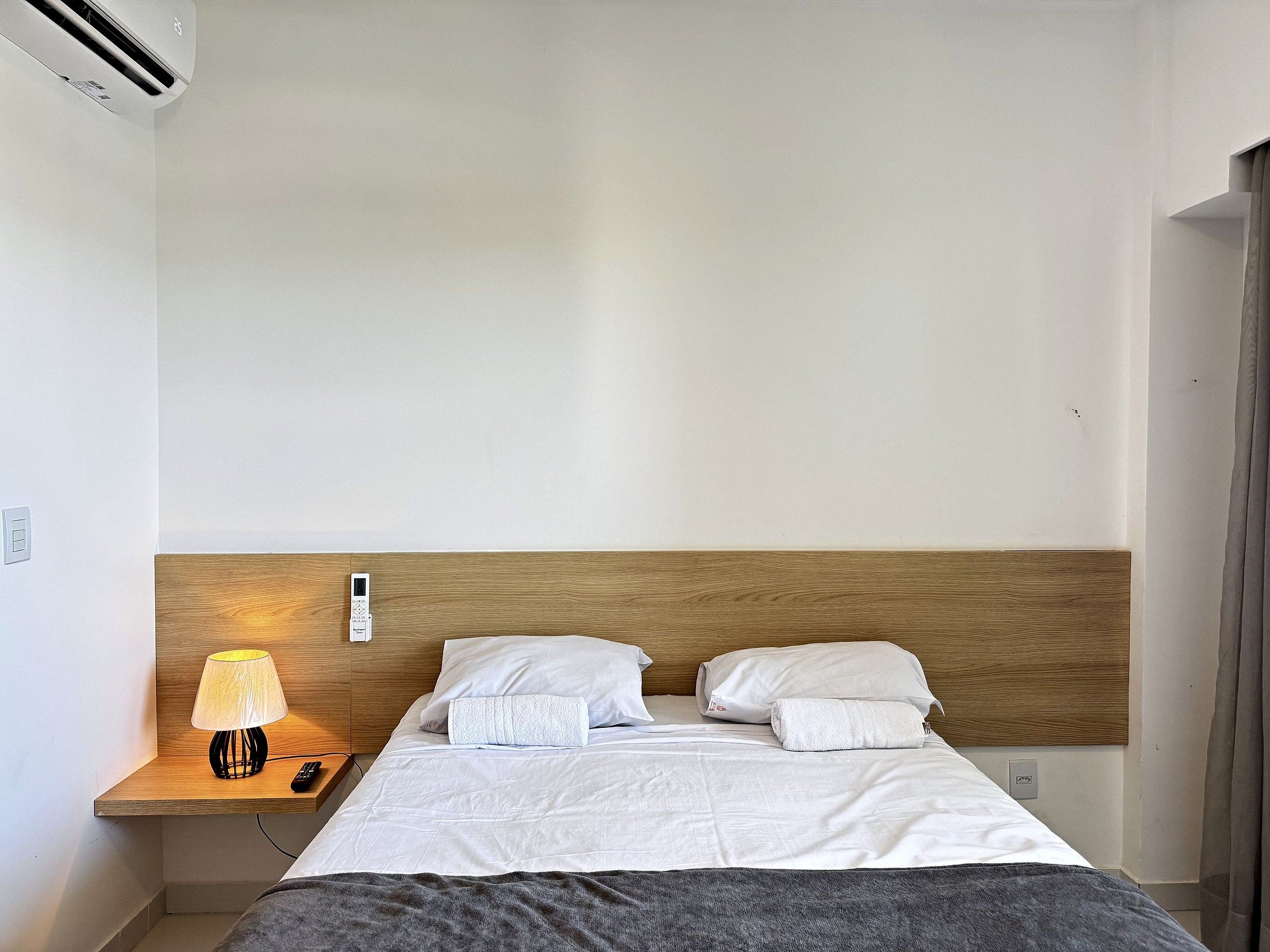 Una habitación de hotel con cabecera de madera, una mesita de noche con lámpara y una cama con ropa blanca.