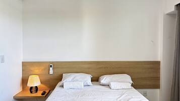 Una habitación de hotel con cabecera de madera, una mesita de noche con lámpara y una cama con ropa blanca.