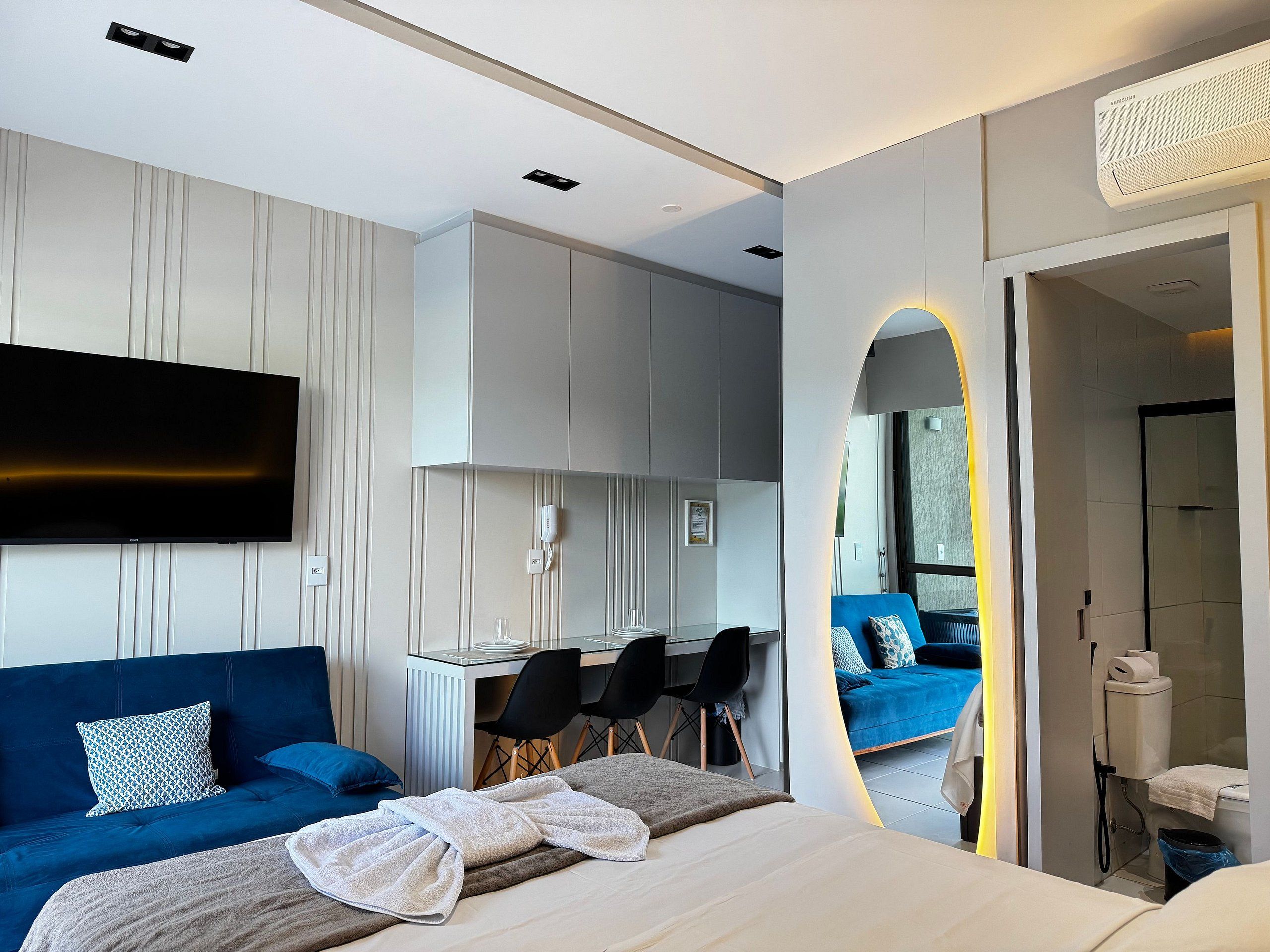 A modern hotel room with a bed, a desk, a TV, and a bathroom.