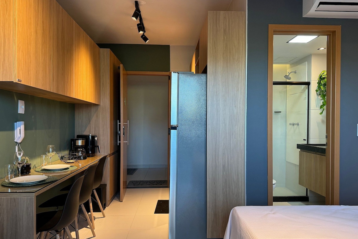 A modern hotel room with a bed, a desk with chairs, a shower area, and a view of the bathroom.