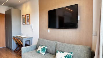 Uma sala de estar moderna com um sofá cinzento, duas almofadas decorativas, uma TV de tela plana na parede, uma mesinha com tampo de vidro e piso de madeira.