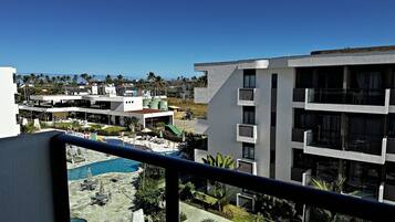 A multi-story building with balconies, a swimming pool, and a view of palm trees and other buildings.
