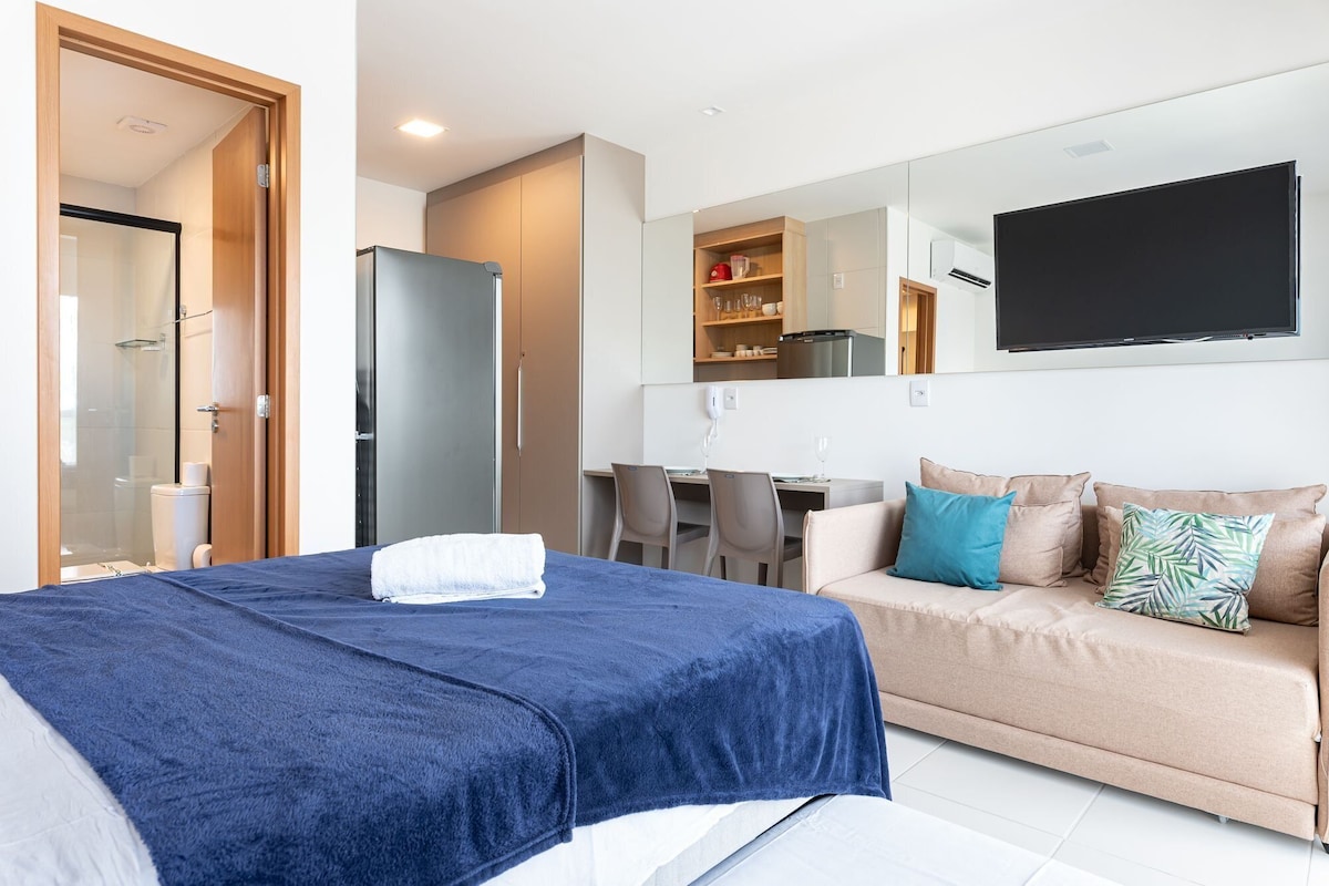 A modern hotel room with a bed, a sofa, a dining area, and a TV.