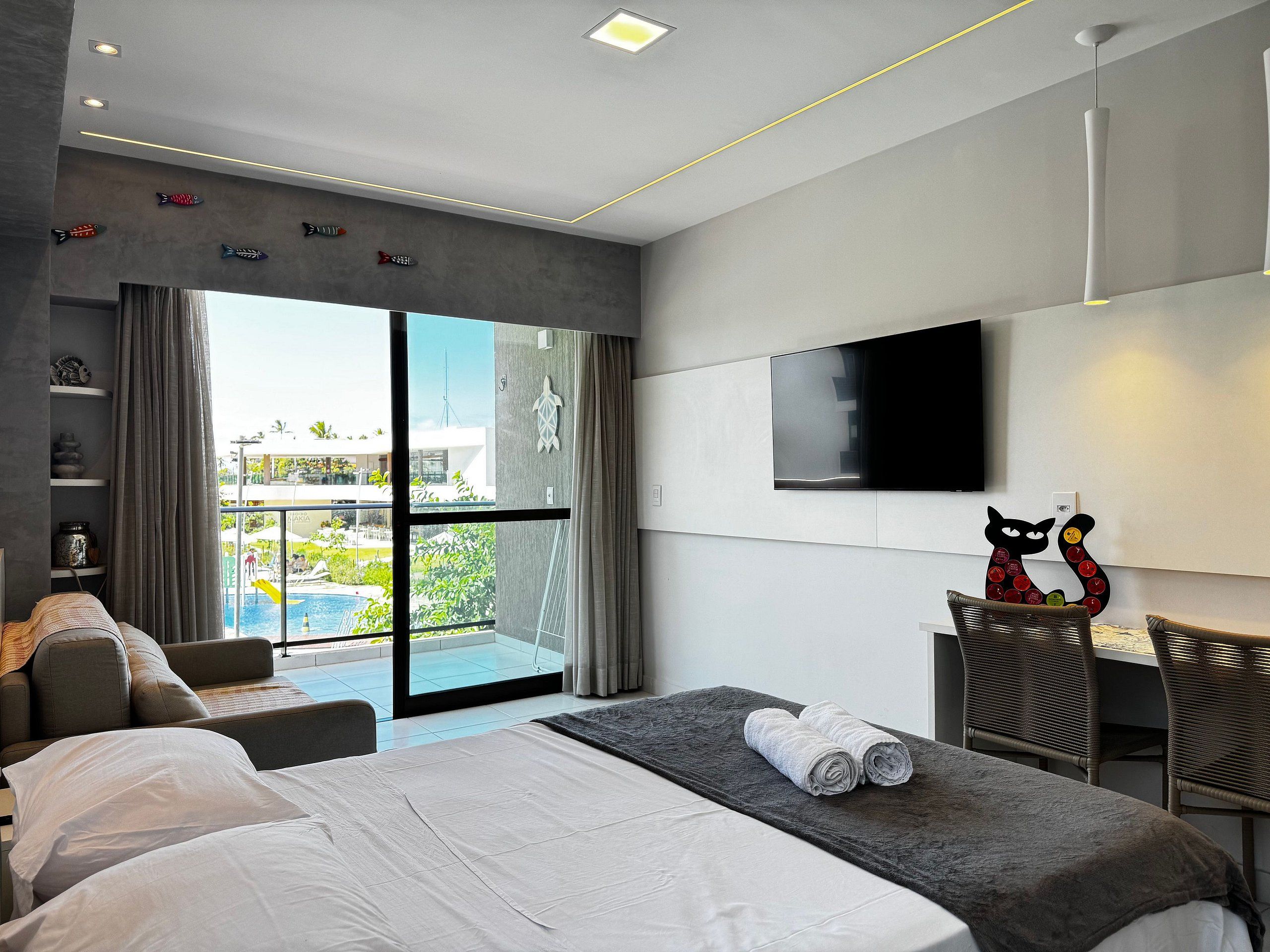 Ein modernes Hotelzimmer mit Bett, Fernseher, einem Balkon mit Blick auf den Pool und einem Essbereich.