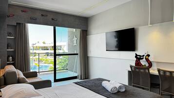 Ein modernes Hotelzimmer mit Bett, Fernseher, einem Balkon mit Blick auf den Pool und einem Essbereich.
