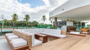 Uma área de estar moderna ao ar livre, com vista para a piscina, incluindo um sofá, cadeiras e uma mesa de jantar.