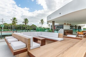 A modern outdoor seating area with a pool view, including a sofa, chairs, and a dining table. - Makia Beach Experience Muro Alto (Ipojuca)