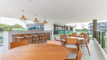 Uma área de refeições moderna com uma mesa redonda de madeira e cadeiras, um balcão de bar e iluminação pendente.