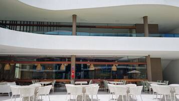 A modern building with a glass facade, outdoor seating area with white wicker furniture, and a clear sky.