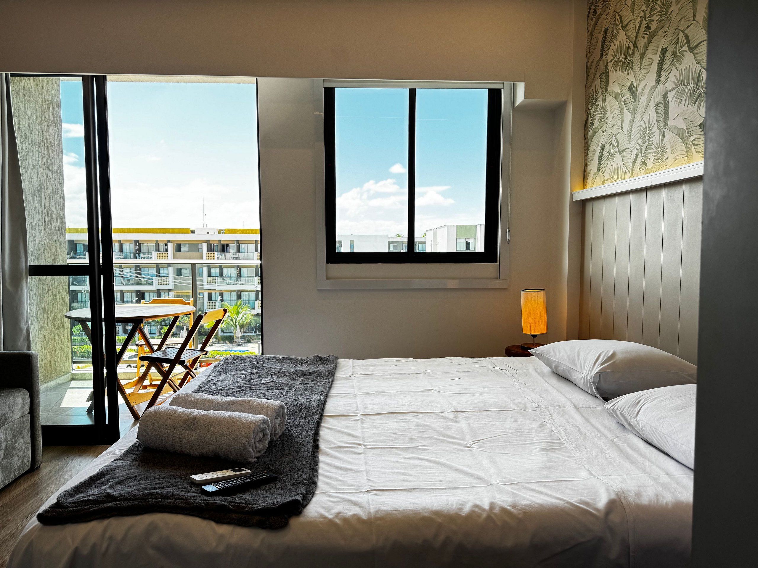 Ein Schlafzimmer mit einem Bett, einem Fenster, einem Tisch mit Stühlen und Blick auf Gebäude.