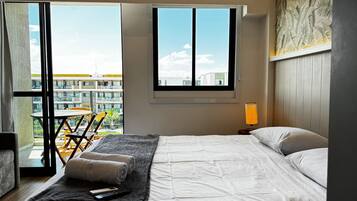 Ein Schlafzimmer mit einem Bett, einem Fenster, einem Tisch mit Stühlen und Blick auf Gebäude.