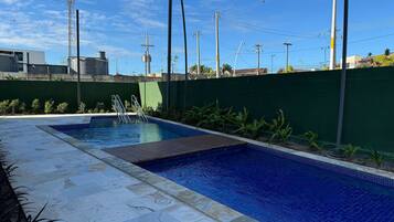 Una piscina con solárium empedrado, rodeada por un muro verde y plantas.