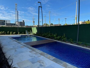 Una piscina con solárium empedrado, rodeada por un muro verde y plantas.