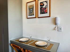 Un comedor con una mesa dispuesta para dos personas, una obra de arte enmarcada encima y un teléfono en la pared.
