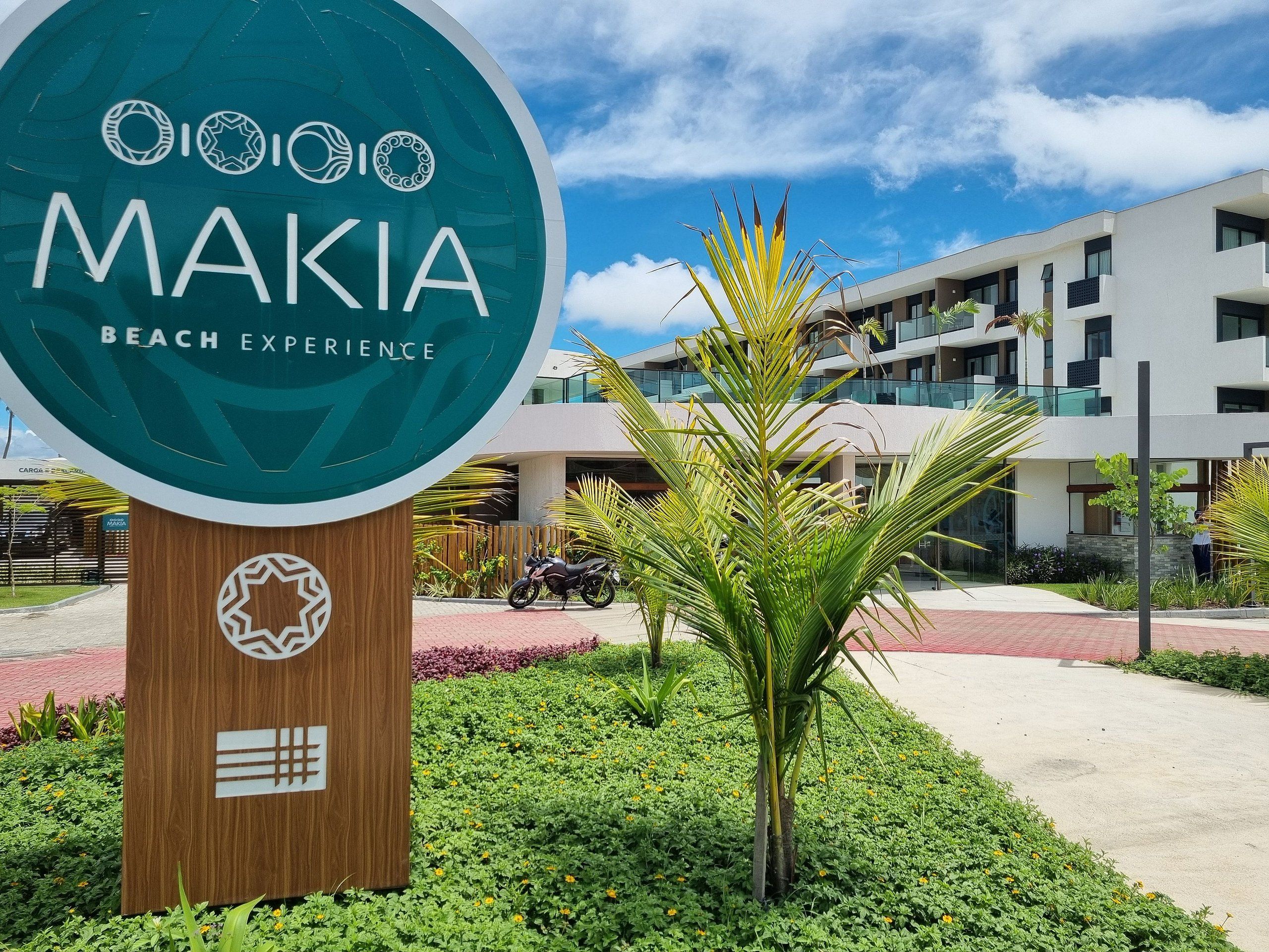 A sign for Makia Beach Experience with a modern building in the background.