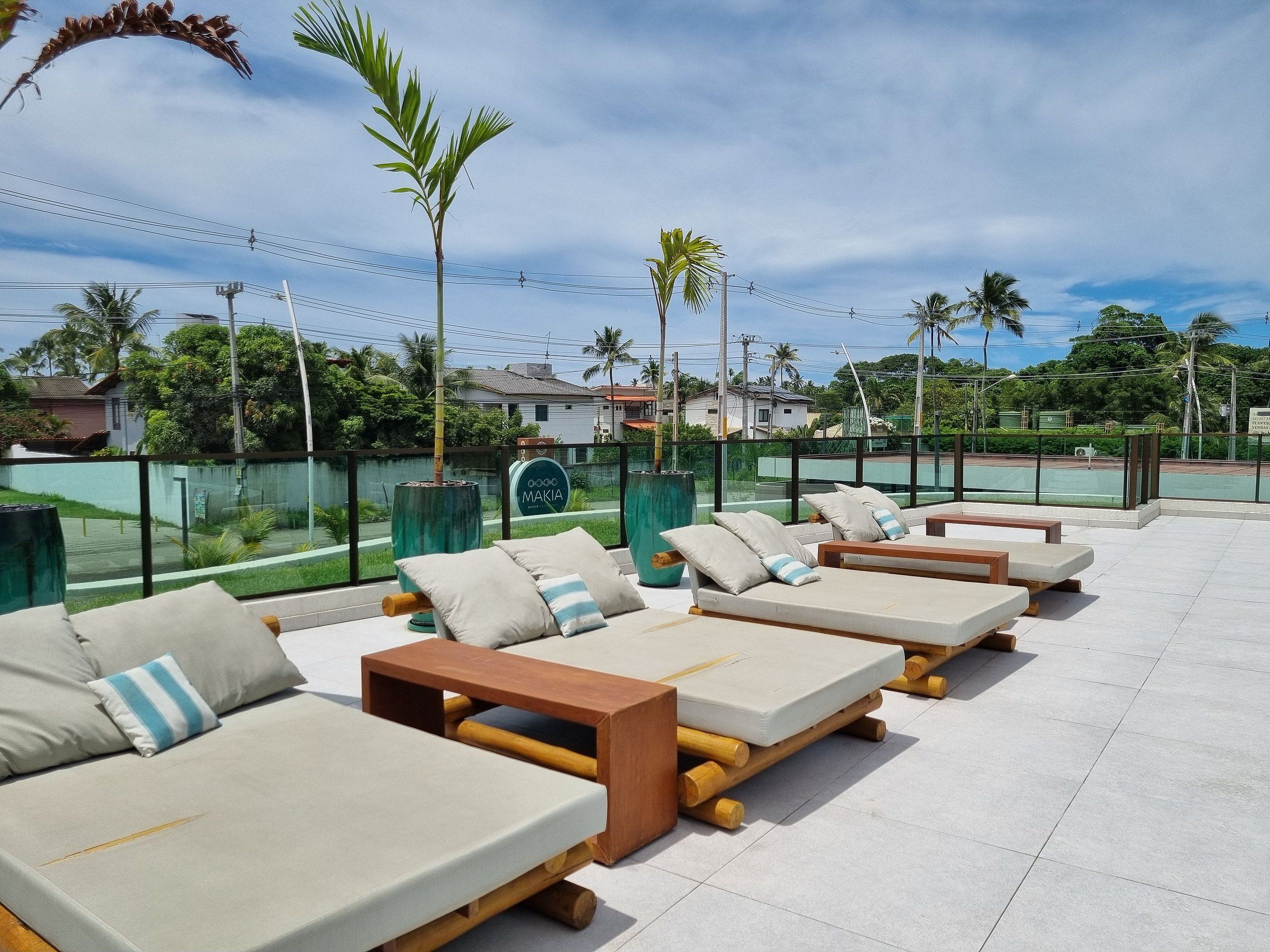 A rooftop lounge area with sun loungers, a sign for 'Makia', and a view of the surrounding greenery and buildings.