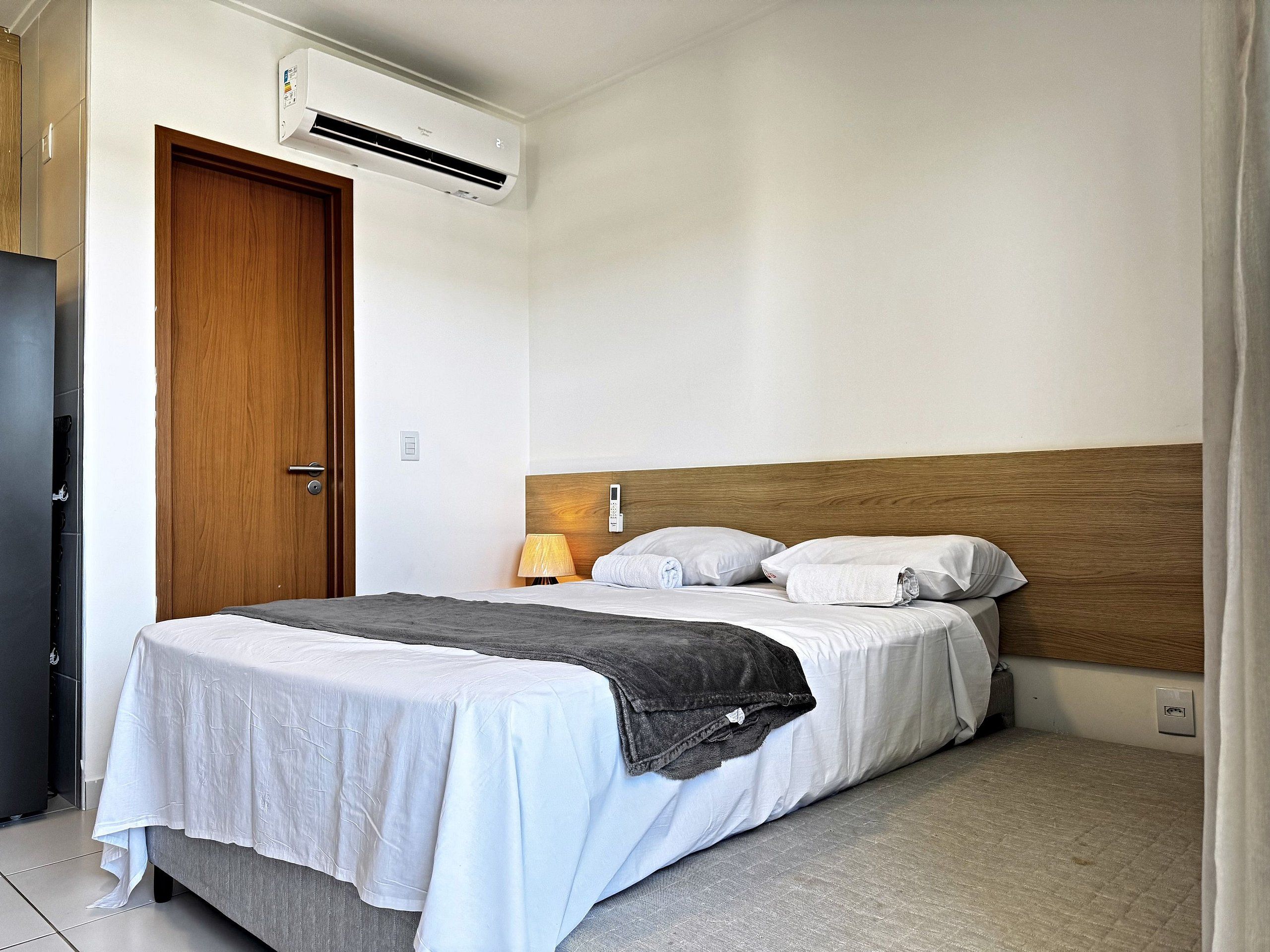 Habitación de hotel con una cama, una mesita de noche, una lámpara, un equipo de aire acondicionado y una puerta.