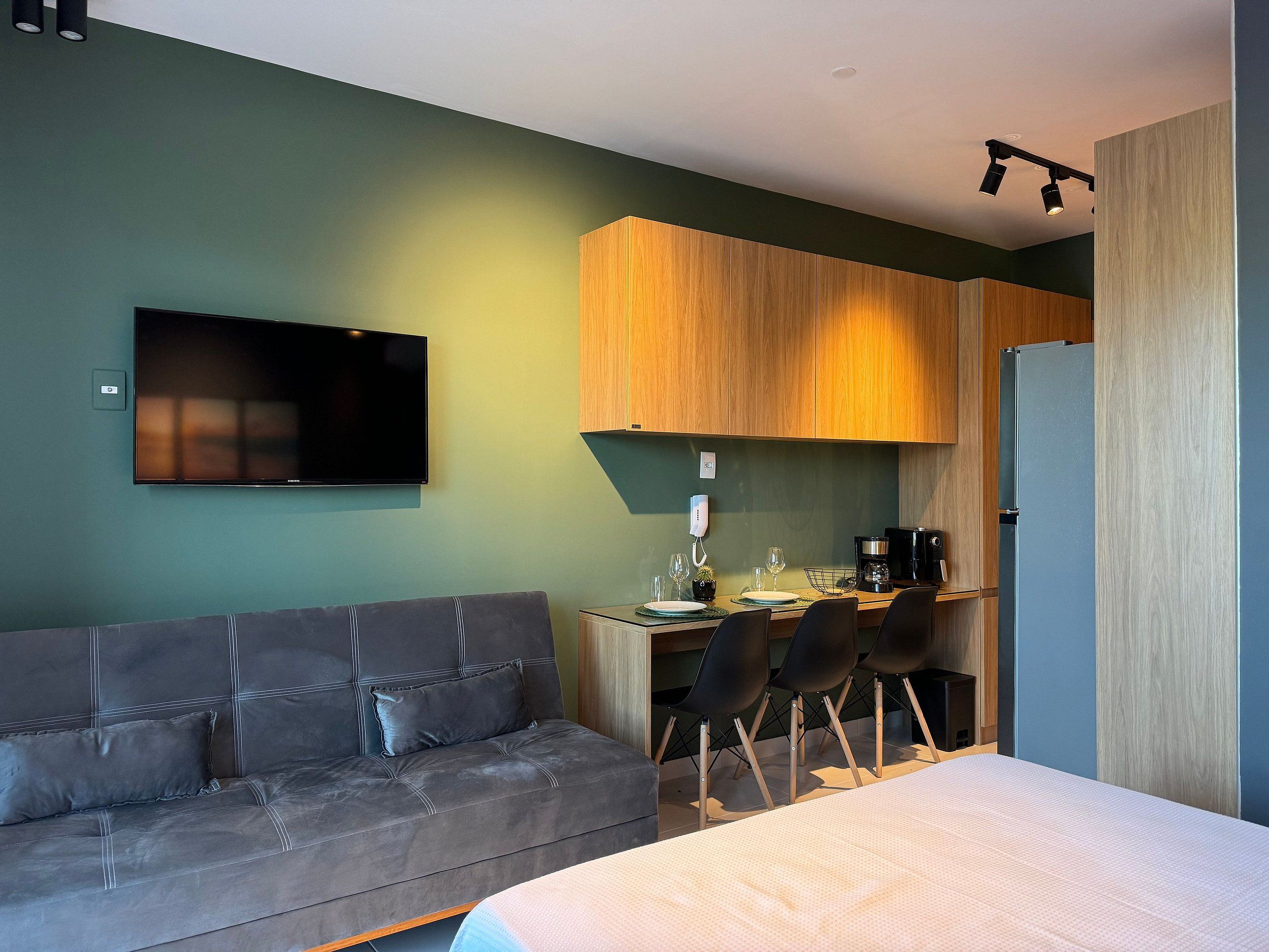 Ein modernes Zimmer mit einer Couch, einem Bett, einem Schreibtisch mit Stühlen, einem Fernseher und einer Küchenzeile.