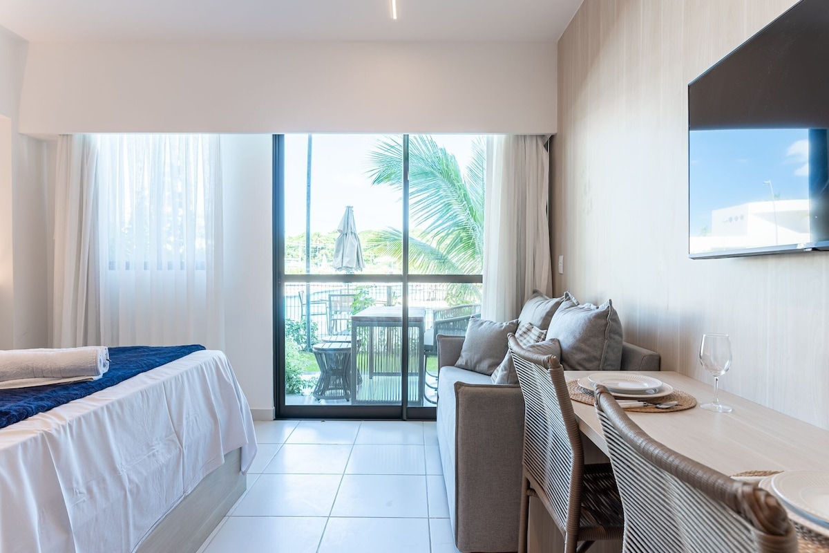 A hotel room with a bed, a sofa, a dining table, and a TV mounted on the wall.